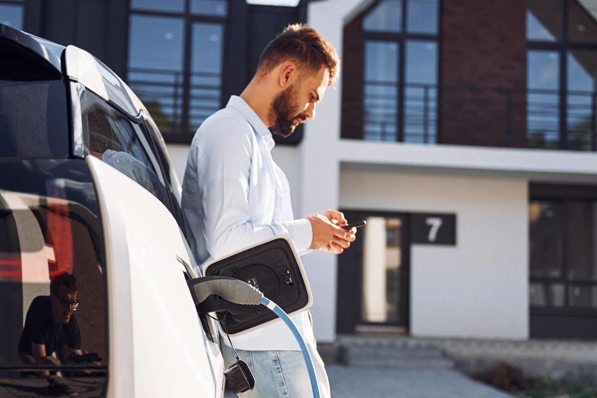 Process of charging the vehicle. Young stylish man is with electric car at daytime