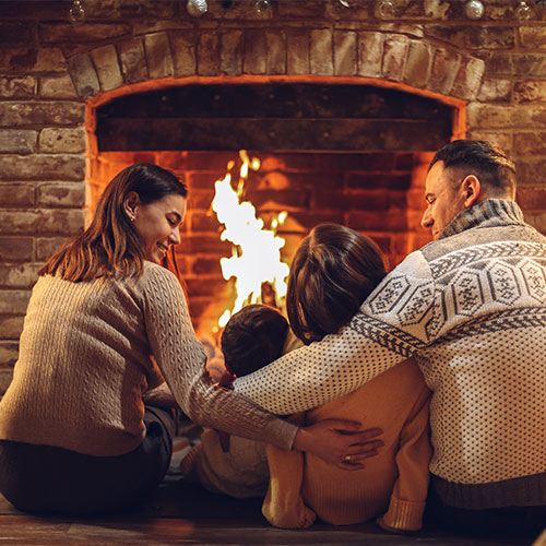 Happy young family parents with two small kids gathering around brick fireplace