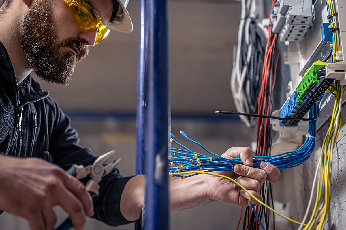 A male electrician works in a switchboard with an electrical connecting cable.