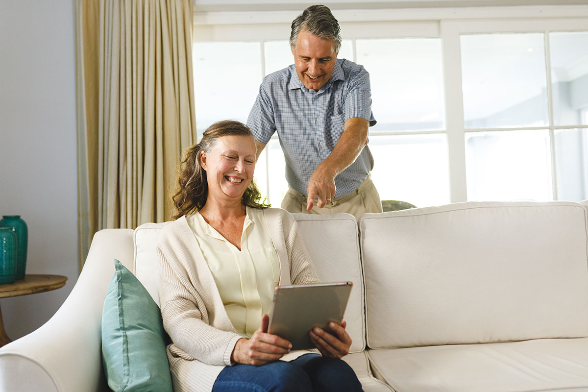 Happy senior caucasian couple in living room, sitting on sofa, using tablet