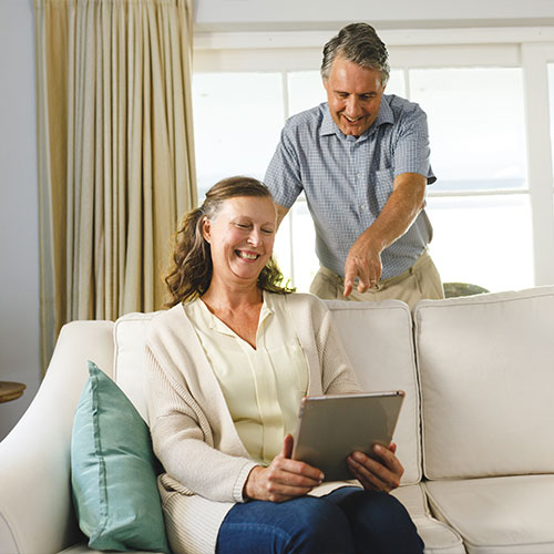 Happy senior caucasian couple in living room, sitting on sofa, using tablet