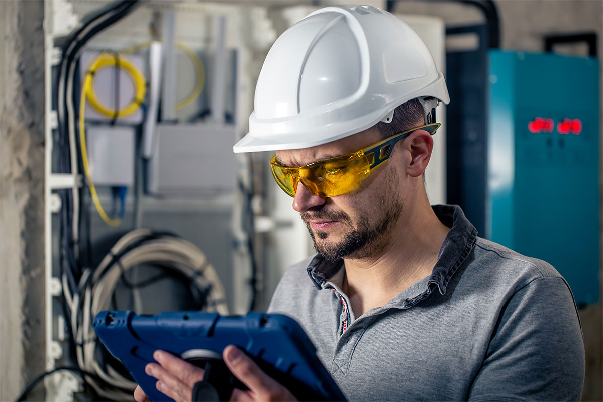 Man, an electrical technician working in a switchboard with fuses, uses a tablet - featured